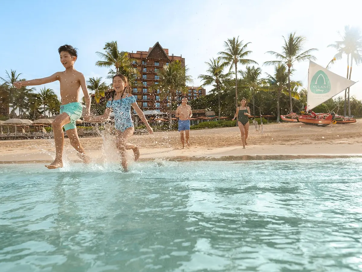 A family splashing in the lagoon in front of Aulani, a Disney Resort & Spa in Hawaii