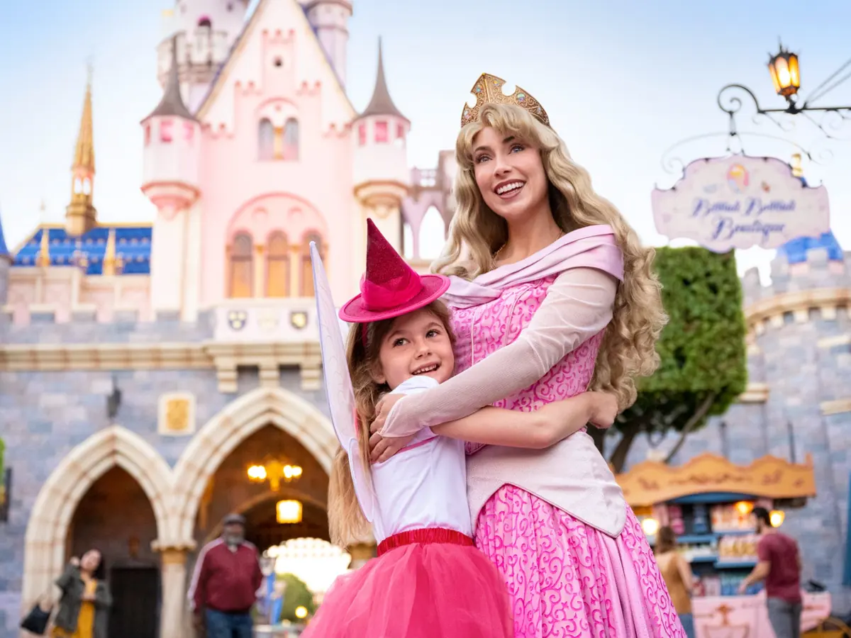 A young girl hugging Princess Aurora in front of Sleeping Beauty Castle at Disneyland